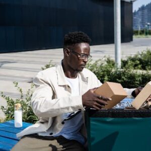 A delivery man sitting outdoors organizing parcels from a thermal bag on a bench.