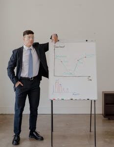 Man in a suit presenting on a whiteboard in a modern office, emphasizing business concepts.