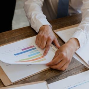 Professional setting with hands pointing at a colorful business chart on paper.