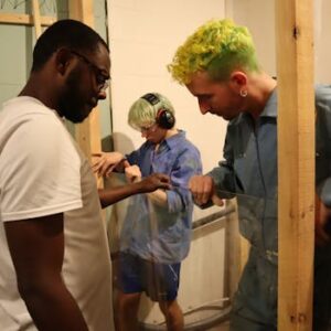 Team of diverse adults working together to install glass in a construction setting.