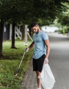 A man picking up litter with a grabber tool in a park, promoting environmental awareness.