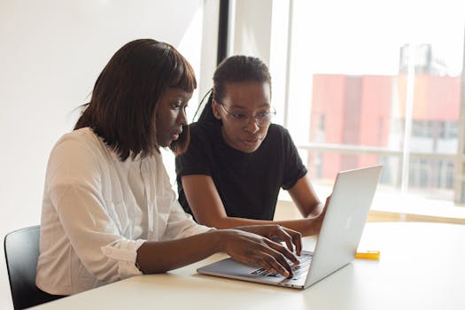 Two office professionals collaborating on a laptop, enhancing teamwork and cooperation.