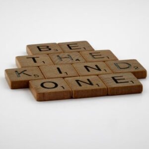Wooden Scrabble tiles spelling 'Be The Kind One' with focus on words and white background.