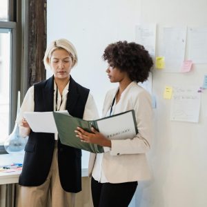 Two professional women reviewing documents in a modern office setting.