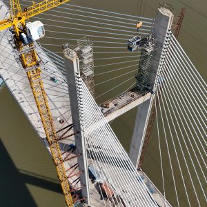 Aerial glance at a cable-stayed bridge under construction, showcasing yellow crane work over a river.