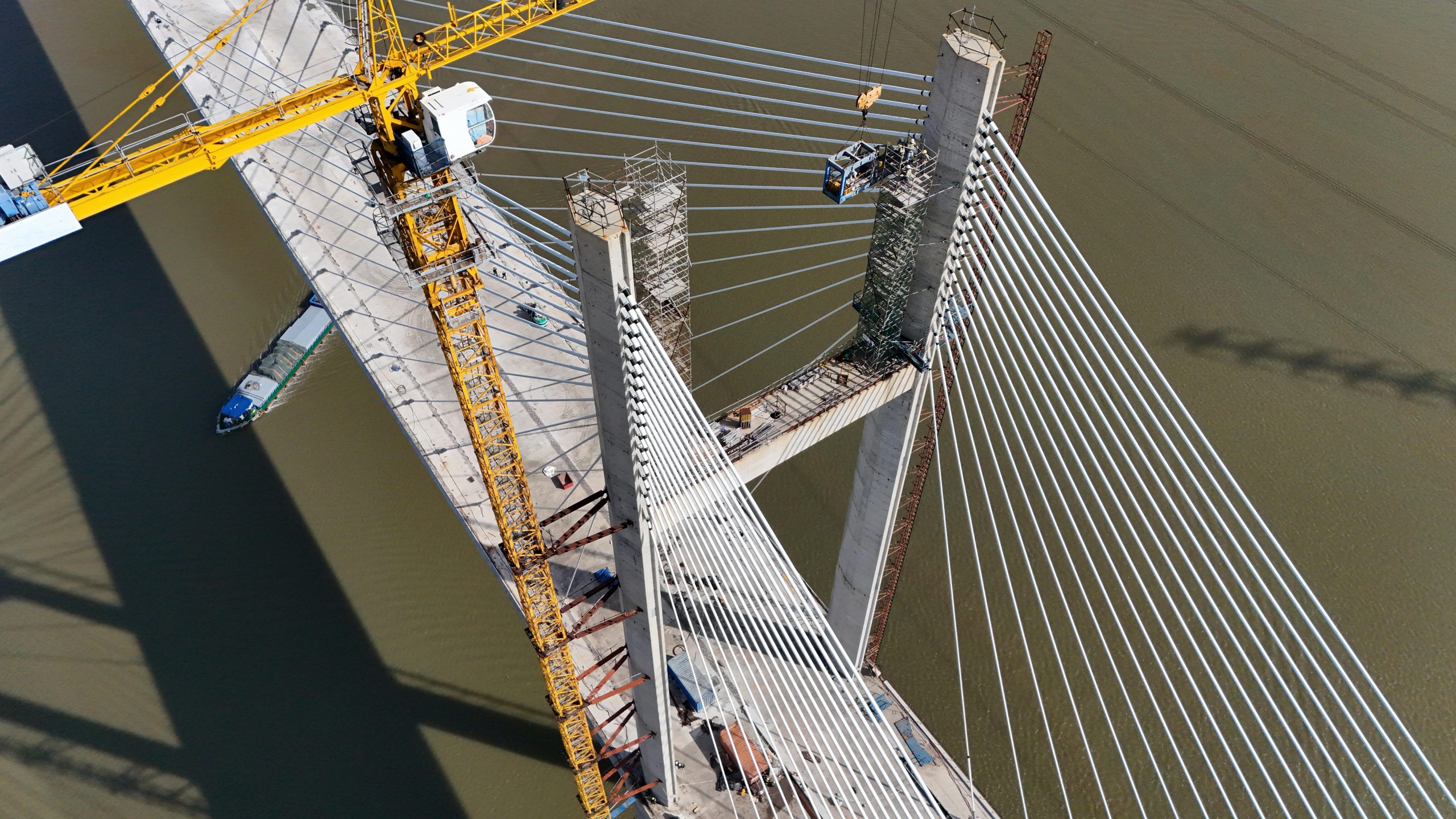 Aerial glance at a cable-stayed bridge under construction, showcasing yellow crane work over a river.