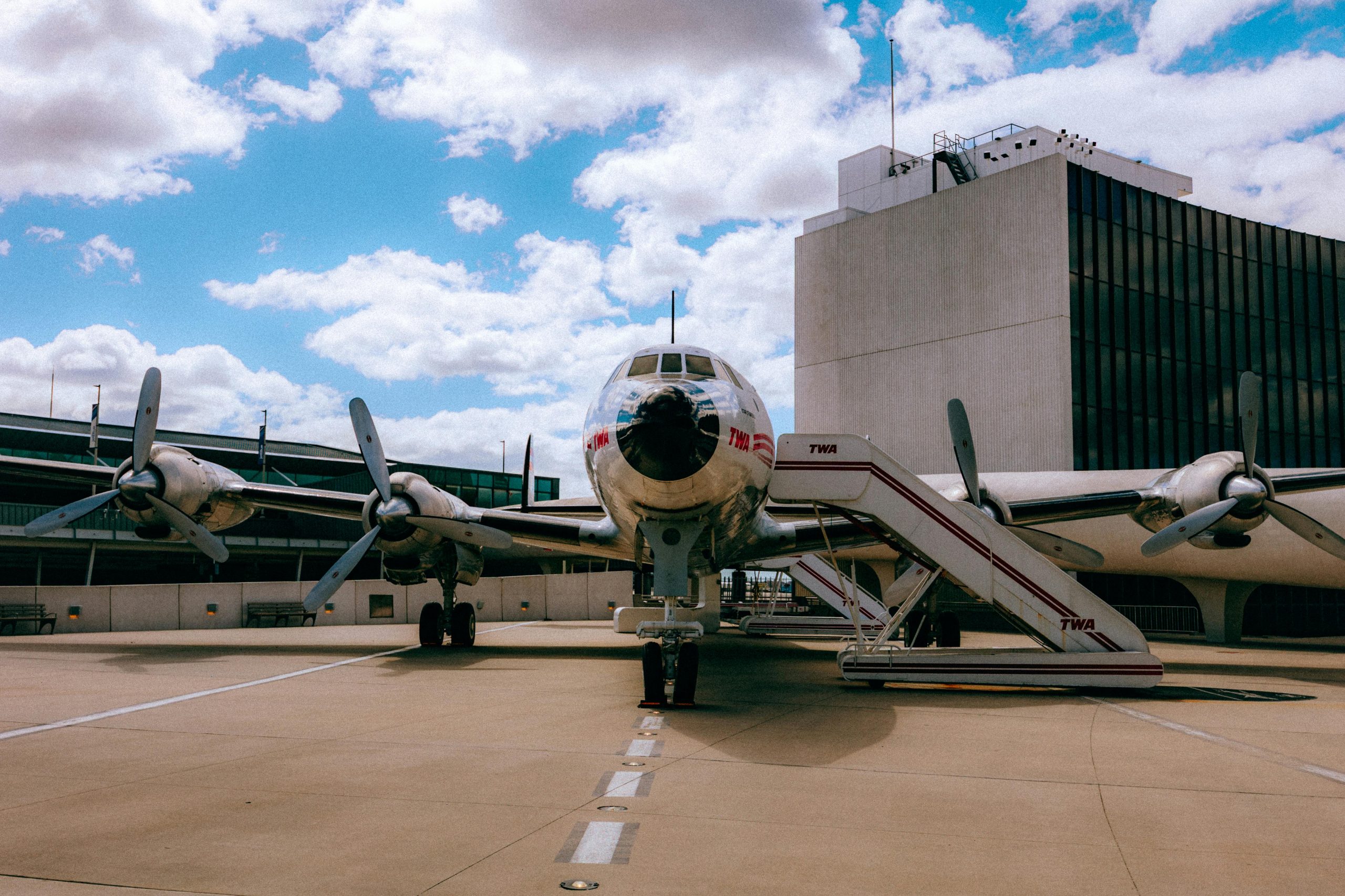 Retro TWA airplane on tarmac with terminal backdrop under blue sky in New York.