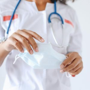 Close-up of a healthcare worker with a stethoscope holding a face mask, emphasizing safety.