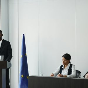 Professional business conference with EU flag, diverse speakers in suits discussing diplomacy.