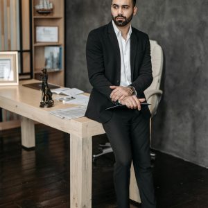 Confident man in formal suit leaning on office desk, showcasing a professional setting.