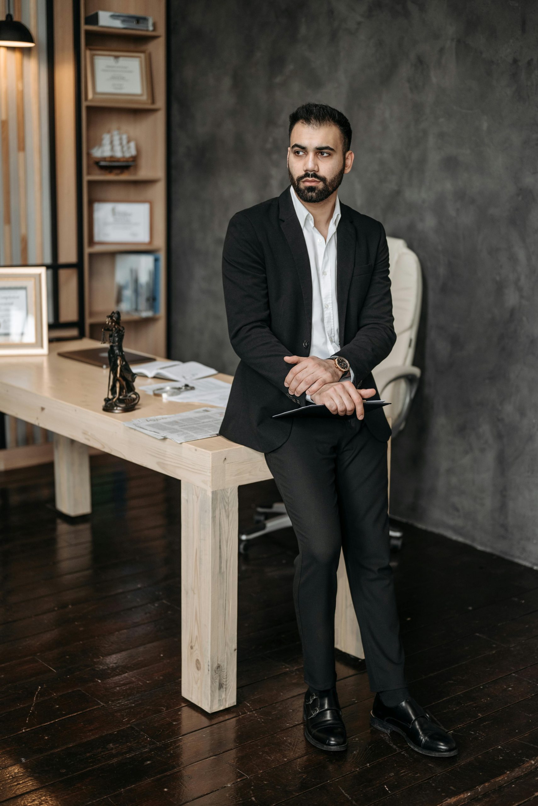Confident man in formal suit leaning on office desk, showcasing a professional setting.