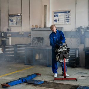 A mechanic repairing a car engine in a busy auto repair shop with tools around.