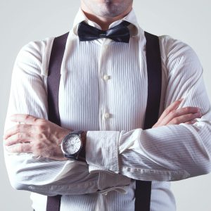 A stylish man crossing his arms, dressed elegantly in a bow tie and suspenders.
