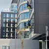 Two workers clean windows on a tall office building in a city setting.