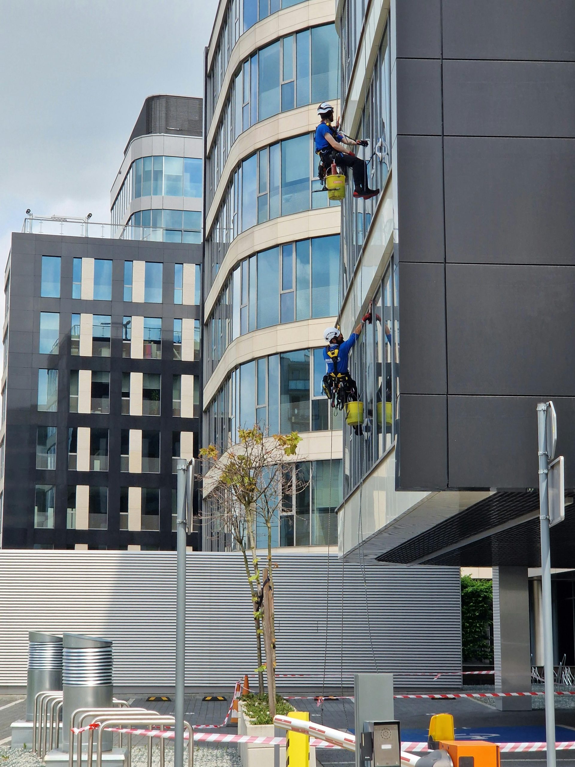 Two workers clean windows on a tall office building in a city setting.