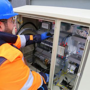 Engineer in safety gear working on an outdoor electrical panel, ensuring system functionality.