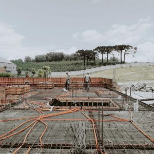 Outdoor construction site with visible steel framework and workers, set against a clear sky.