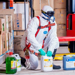 Industrial worker in protective gear handling chemicals in a warehouse environment.