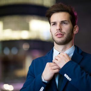 Portrait of a stylish businessman adjusting his suit in an urban night setting.