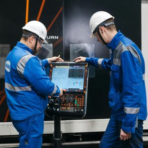 Two engineers operating CNC machinery in a factory setting, wearing safety gear and uniforms.