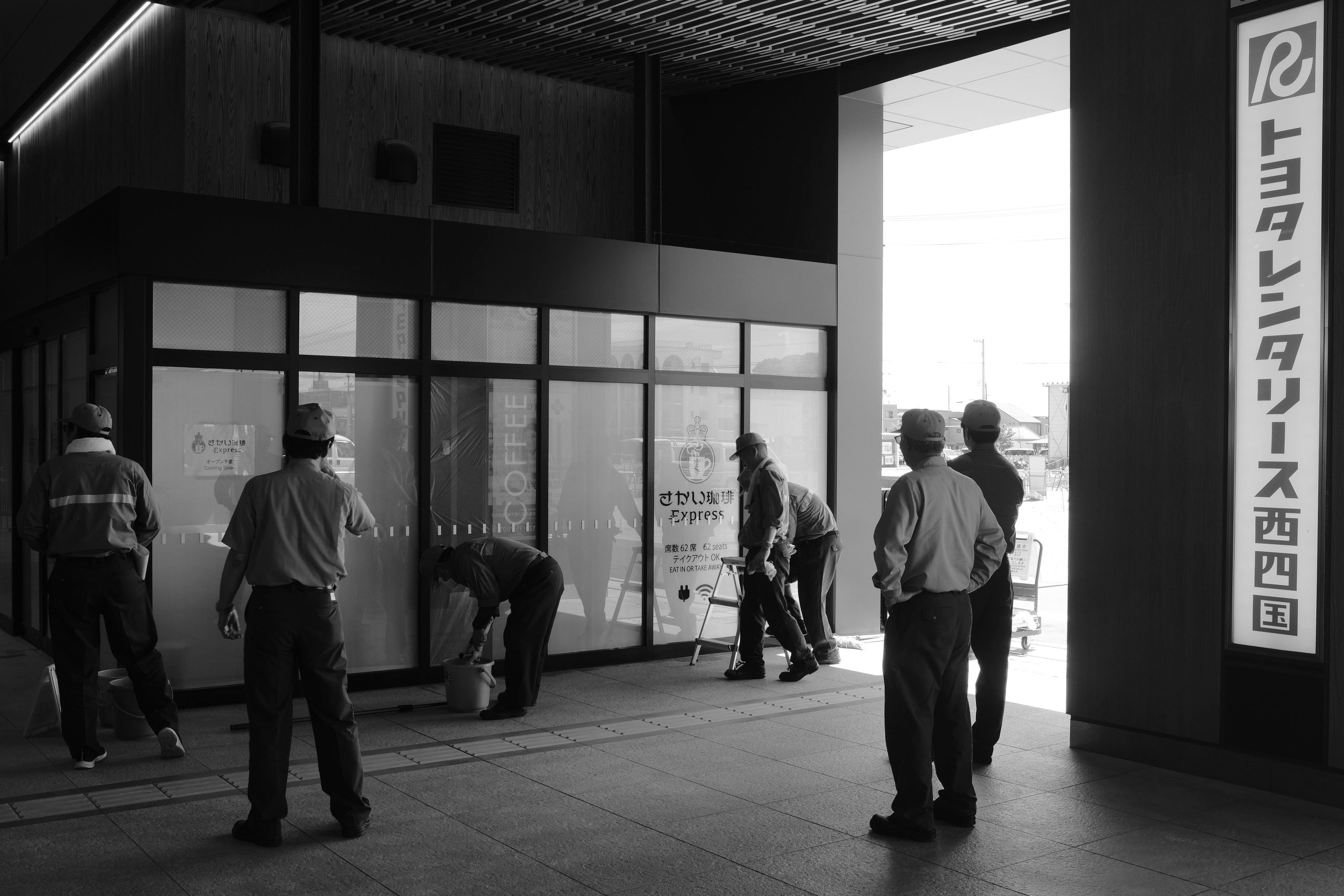 Workers maintaining cleanliness at a Japanese station in black and white.