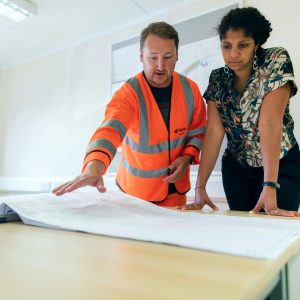 Two engineers reviewing blueprints in an office, discussing project details.