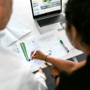 Engineers collaborate on designs with blueprints and laptops in a modern office setting.