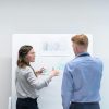 Two professionals discussing project plans at whiteboard in office setting.