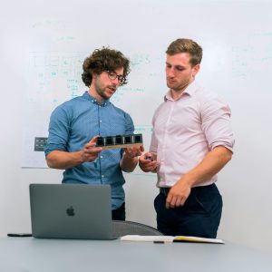 Two men in an office discussing and reviewing a tech prototype.