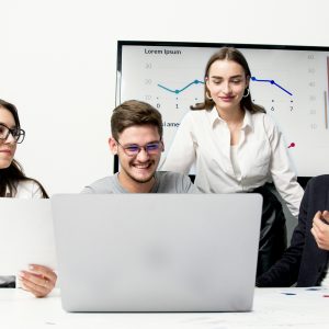A group of young professionals collaborating in an office meeting, discussing ideas with a laptop and charts.