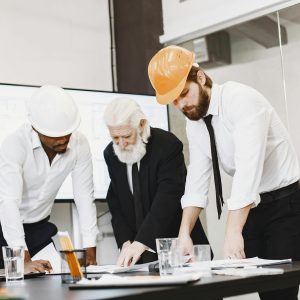 Group of architects discussing construction blueprints wearing hardhats in a modern office.