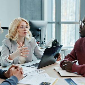 Business professionals discussing strategy around a table with a laptop in an office setting.