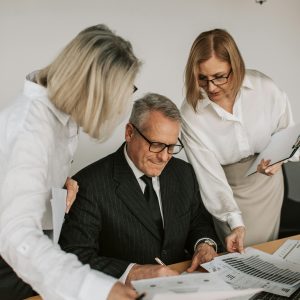 A senior businessman with colleagues discussing documents in a modern office.