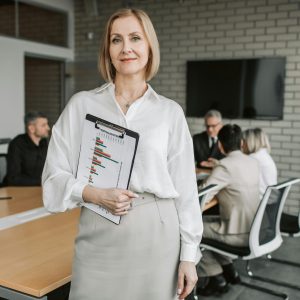 Professional businesswoman holding a clipboard during an office meeting, showcasing leadership in a corporate environment.