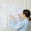 A woman arranging planning documents on an office wall, illustrating business strategy and organization.