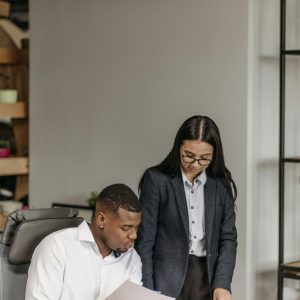 Two colleagues discuss documents during a business meeting in a modern office setting.