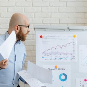 Bald businessman in smart casual attire analyzing financial charts on a whiteboard in an office setting.