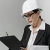 Middle-aged woman architect with eyeglasses and hard hat reviews construction plans indoors.
