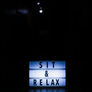 Illuminated sign displaying 'Sit & Relax' on a dark background.