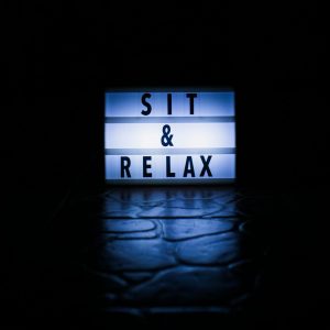 Illuminated sign displaying 'Sit & Relax' on a dark background.