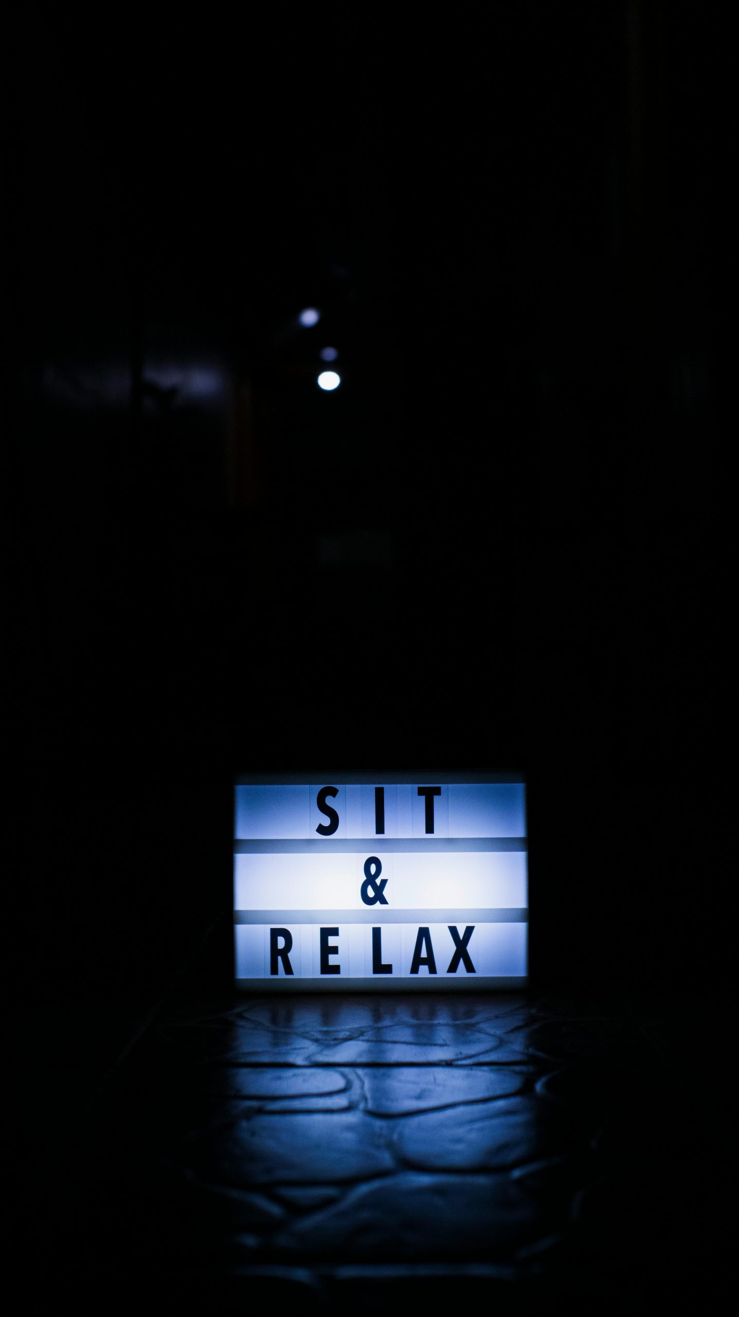 Illuminated sign displaying 'Sit & Relax' on a dark background.