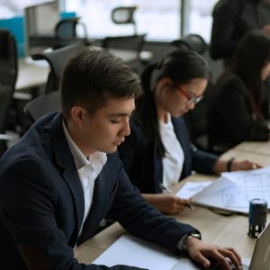 Business professionals working on laptops in an office with a city view, focused and busy.