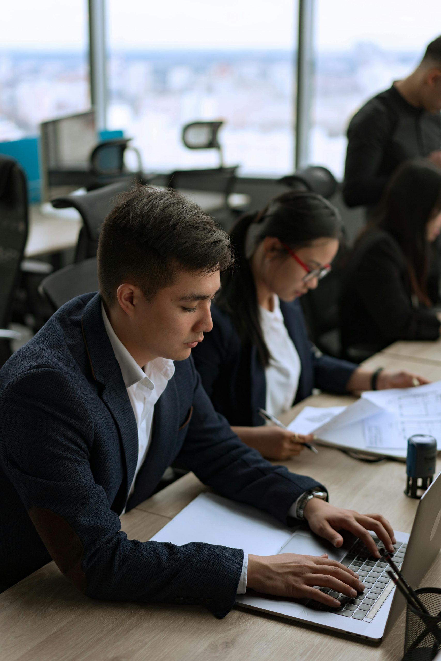 Business professionals working on laptops in an office with a city view, focused and busy.