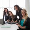 Four businesswomen in a meeting room, collaborating and smiling during a team discussion.