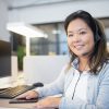 Smiling call center agent wearing a headset while working at her desk in a modern office setting.