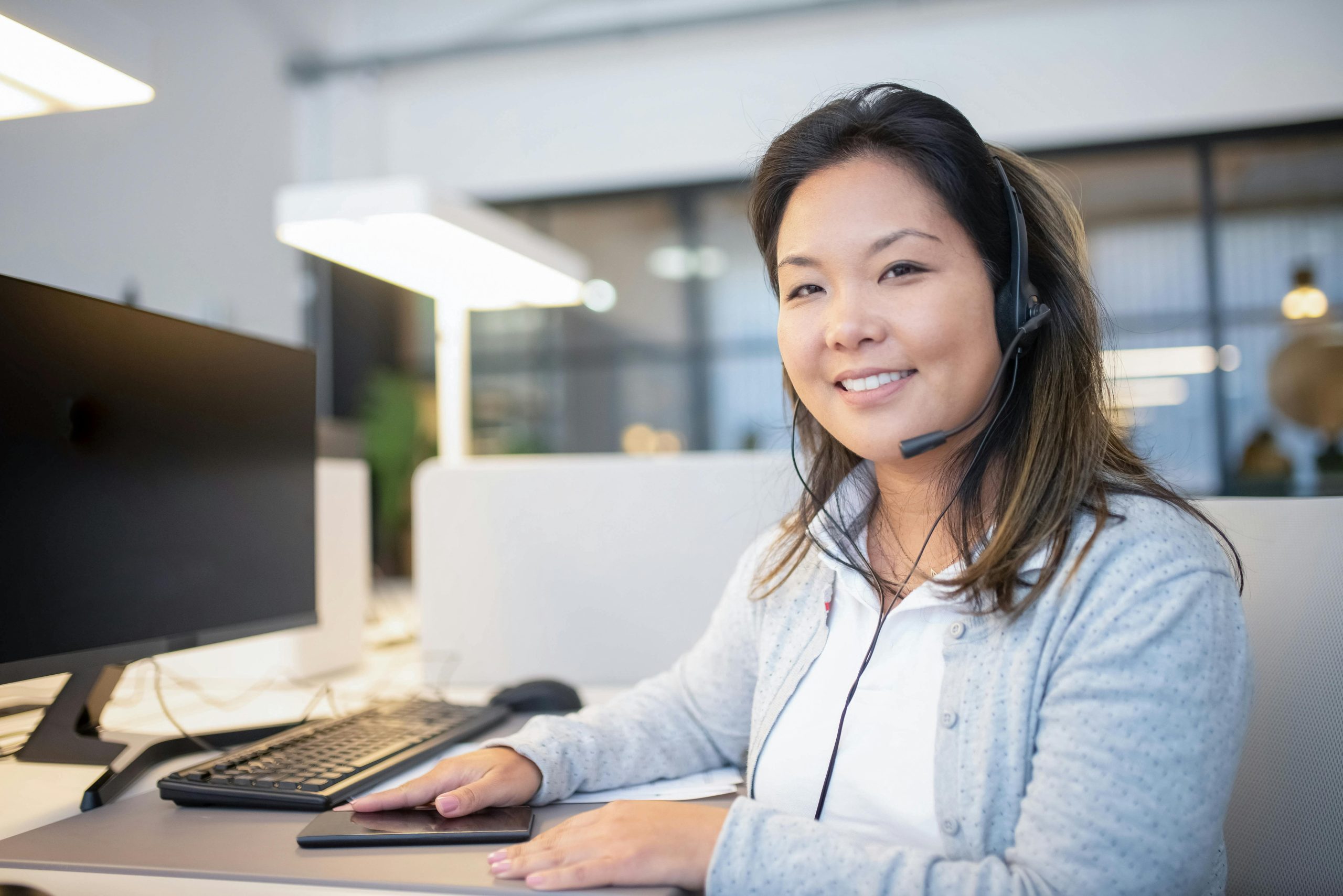 Smiling call center agent wearing a headset while working at her desk in a modern office setting.