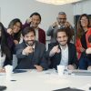 A diverse group of colleagues smiling and pointing in a modern office setting, promoting teamwork.