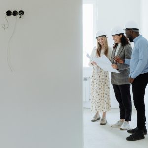 Three architects with hard hats reviewing building plans in an unfinished room.