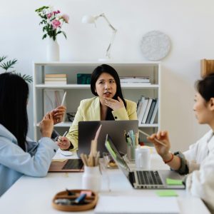 Professional team brainstorming in a modern office setting with laptops and plants.