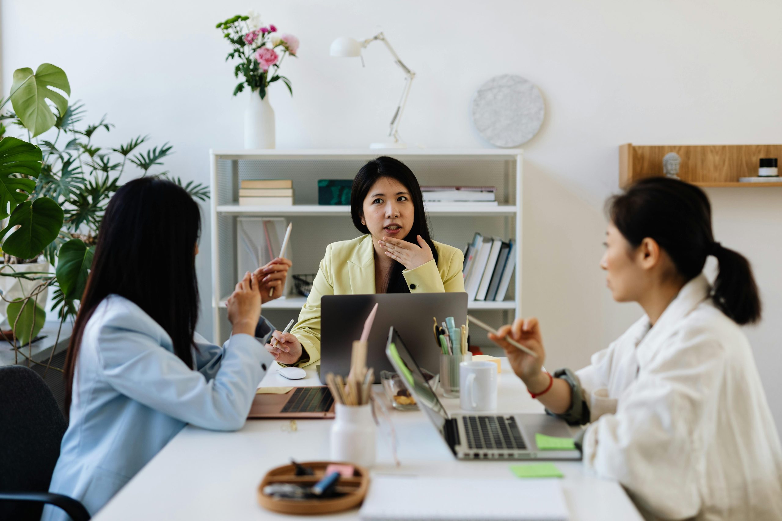 Professional team brainstorming in a modern office setting with laptops and plants.